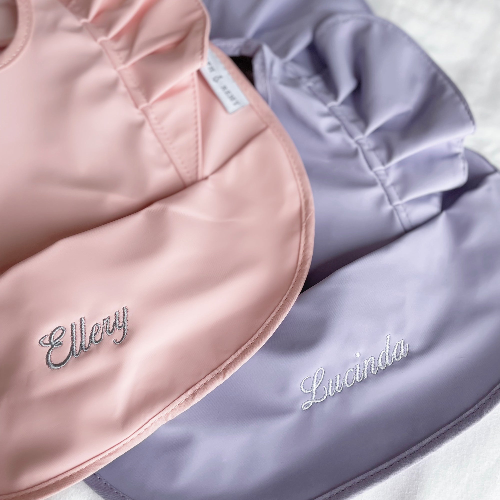 Close-up of customized RAPH&REMY® waterproof bib with baby’s name in pink and purple color
