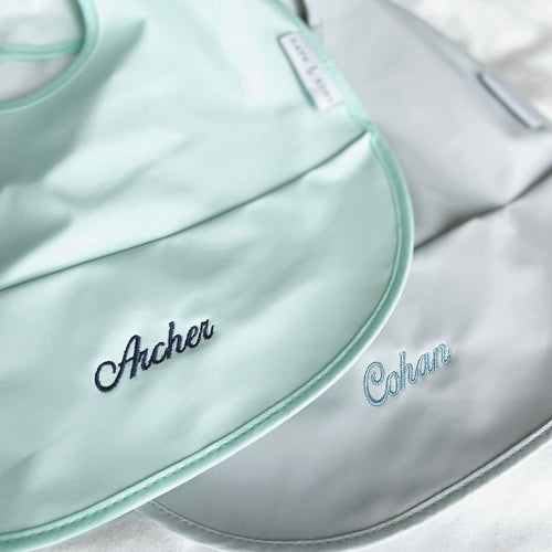 Close-up of customized RAPH&REMY® waterproof bib with baby’s name in green and grey color