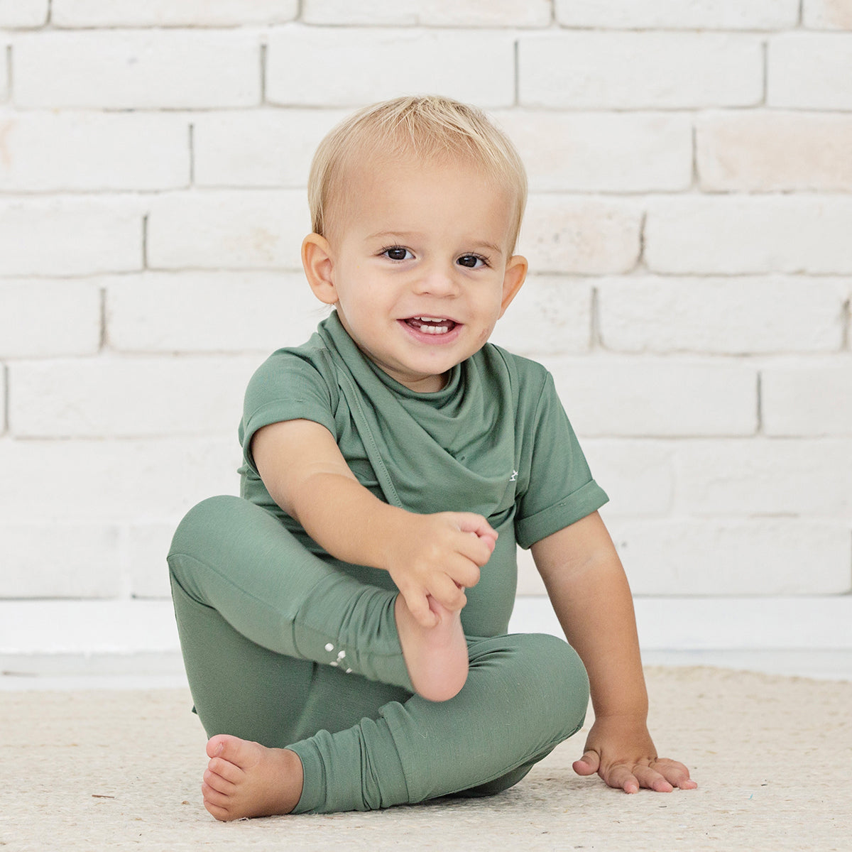 Baby sitting and smiling in Premium Bamboo Bandana Bib by RAPH&REMY® in army green