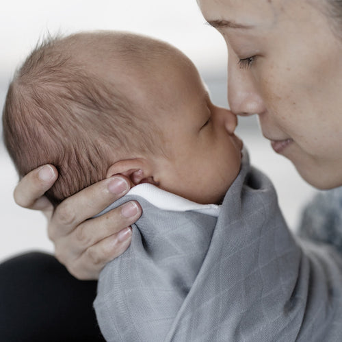Mother kissing newborn in Premium Bamboo Swaddle in Grey by RAPH&REMY®