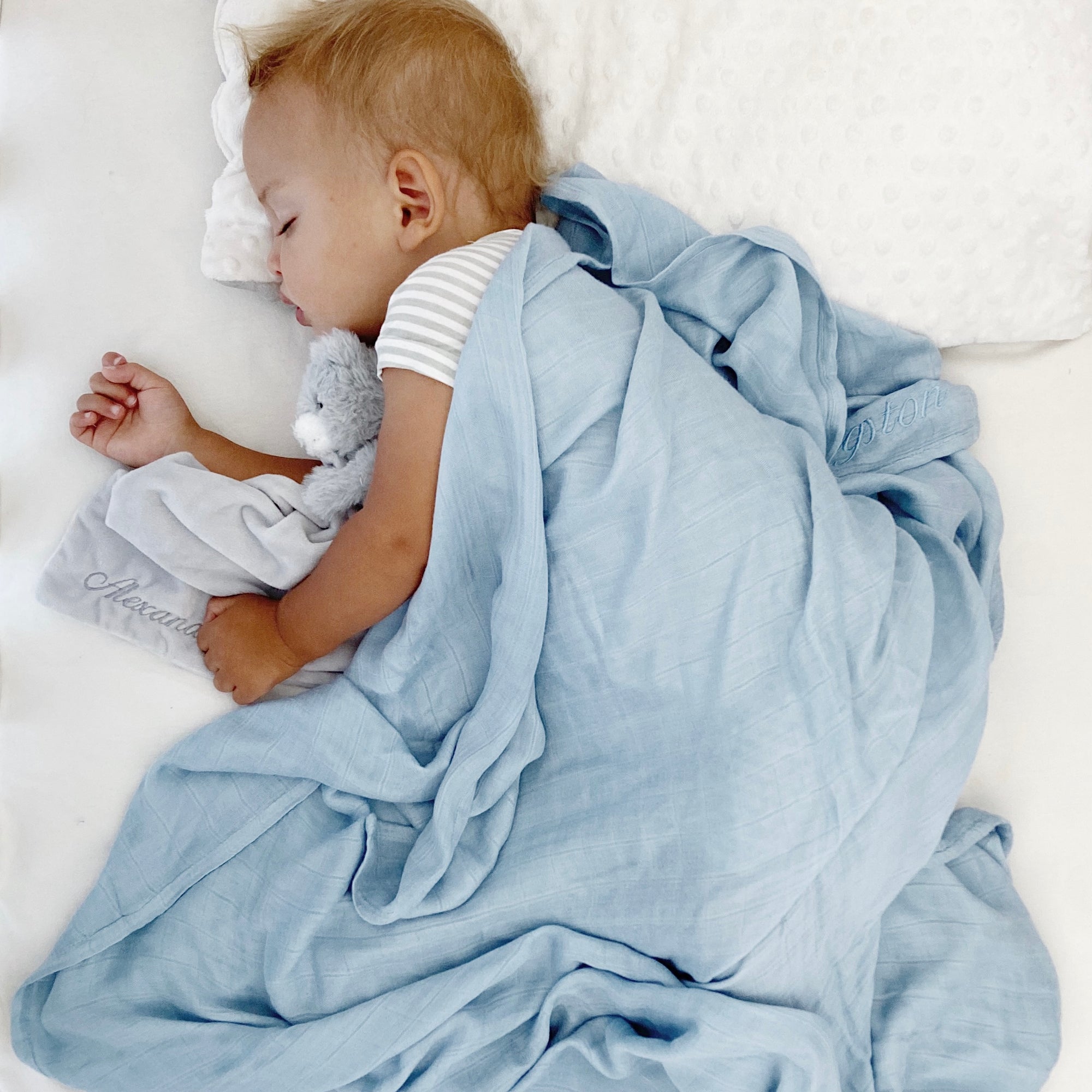 Baby sleeping wearing high-quality swaddle from RAPH&REMY® in light blue color.