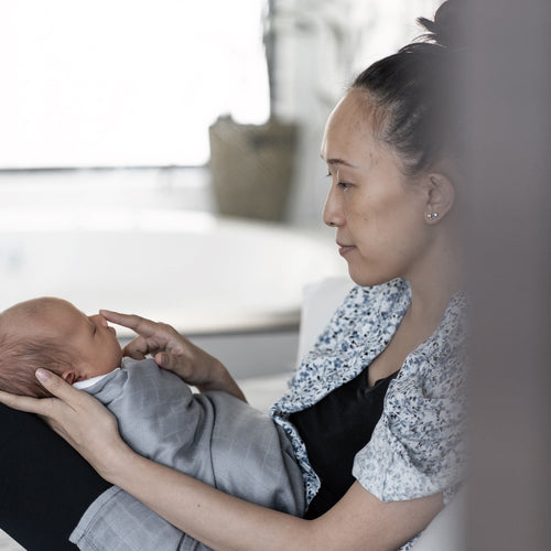 A mother lovingly holding her baby wrapped in a soft bamboo swaddle from RAPH&REMY®, showcasing the swaddle's cozy and elegant design.
